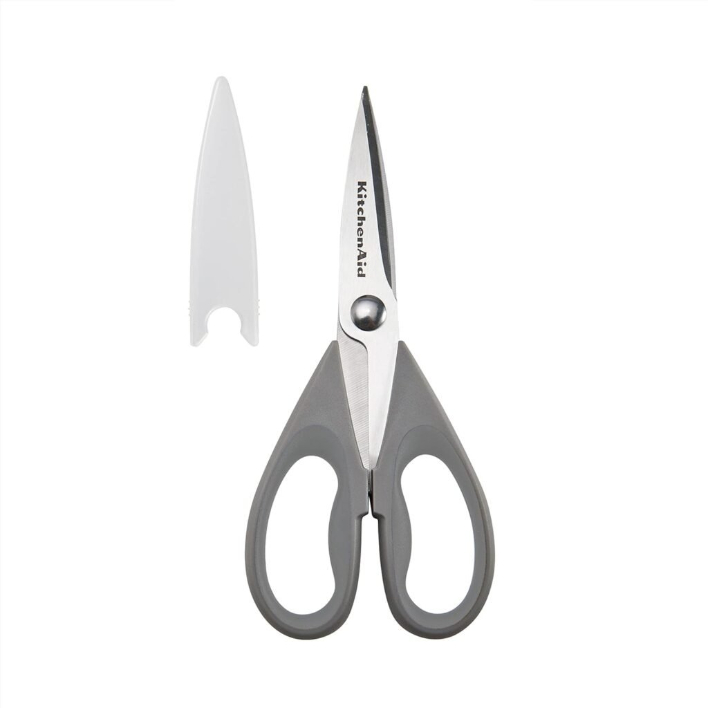 The image shows a pair of KitchenAid All Purpose Shears with a gray handle and stainless steel blades. The shears come with a protective blade cover placed beside them.